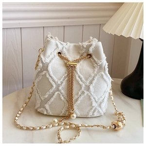 Detail of white denim bucket bag featuring diamond quilting and pearl drawstring accents