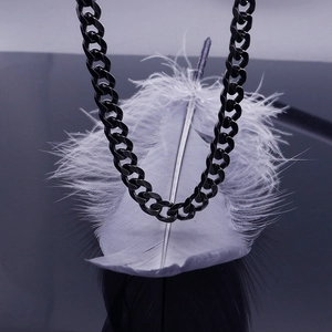 Detailed close-up of a black titanium steel Cuban chain necklace over a white feather