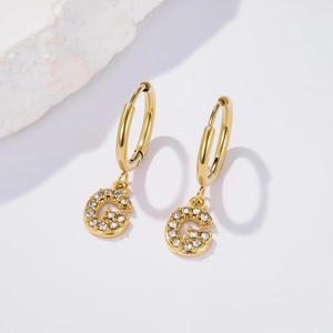 Detail of gold huggie hoop earring with crystal-encrusted letter G pendant charm