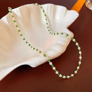 Gold-plated pearl necklace with green beads displayed in a ceramic shell dish