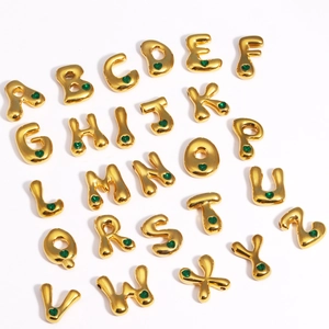 Vue macro de pendentifs alphabet dorés avec pierres de cœur vertes sur fond blanc