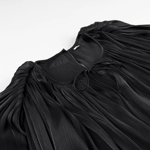 Detail view of black pleated fabric with subtle sheen and elegant neckline ribbon tie