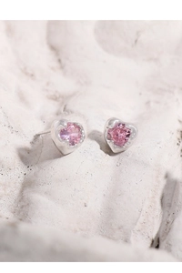 Macro shot of silver heart studs with pink zircon on grey stone textured surface