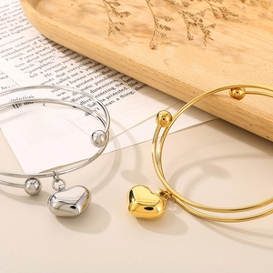 Polished heart charm open bangle bracelets in gold and silver finish on a rustic setting