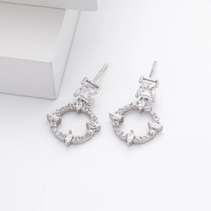 Macro detail of silver earrings featuring square zircons and hollow circular pavé crystals