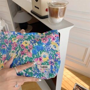 Detail showing hand holding a floral cotton makeup bag in a cozy home setting