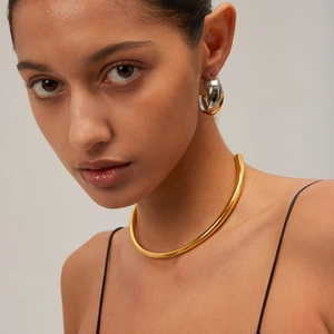 Close-up of model wearing two-tone gold and silver C-hoop earrings and a gold choker