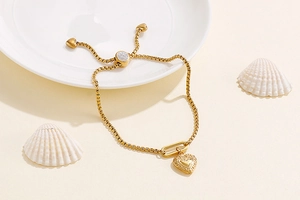 Close-up of golden heart pendant bracelet with adjustable slider chain on a marble tray