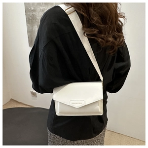 White envelope-style crossbody bag with wide strap worn over a black shirt on model