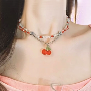 Close-up of double-layer beaded necklace with red cherry pendant and heart links