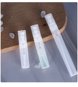 Three clear plastic spray perfume bottles in different sizes on a grey table with petals