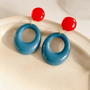 Close-up of red and blue geometric resin earrings on a beige textured ceramic plate