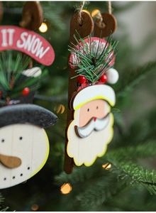 Detail view of wooden Santa Claus and Snowman ornaments with pine needles on a tree