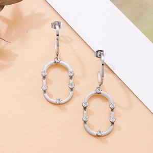 Détail de boucles d'oreilles créoles ovales argentées avec cristaux sur papier texturé