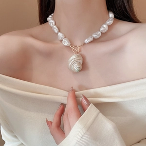 Close-up of elegant baroque pearl necklace featuring a large spiral seashell pendant and T-bar clasp