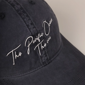 Close-up of white script embroidery on a washed black cotton twill baseball cap