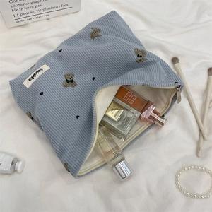 Close-up of light blue corduroy makeup bag featuring bear embroidery and zipper detail