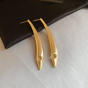 Detailed view of long gold leaf earrings with round cutout design on a leather background