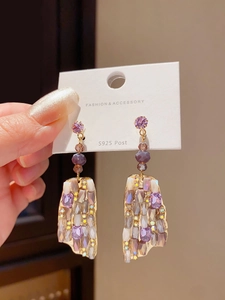 Macro detail of luxury gold-plated earrings featuring purple and clear crystal pavé setting