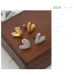 Close-up of gold and silver heart earrings with hammered texture on a wood box