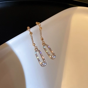 Detailed view of long gold tassel earrings with rhinestone paved oval pendant and chains