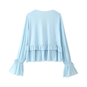 Detail of light blue V-neck top showing ruffle hem and bell sleeves on white background
