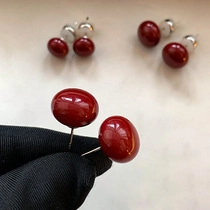 Detail view of round red cabochon stud earrings with silver pins held in black gloves