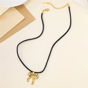 Detailed top view of 18k gold butterfly pendant with black wax cord on a beige desk