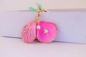 Pink shell keychain with rhinestone inlay and pearl detail on a gold-tone metal ring