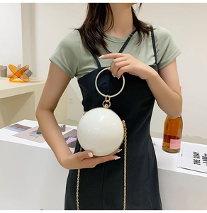 White spherical evening bag with gold rhinestone handle and chain strap on model