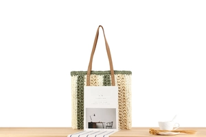 Detail of beige and sage green woven tote bag with brown leather handles on wooden table