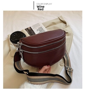 Detail of wine red lychee leather crossbody bag with double zippers and striped strap