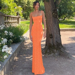 Photo en extérieur d'un mannequin portant une robe longue fleurie orange moulante en jardin