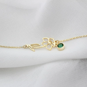 Macro view of a gold floral pendant necklace with a green zircon on white fabric