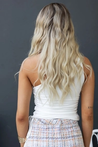 Détail de dos montrant des cheveux blonds ondulés et un haut blanc plissé à épaule