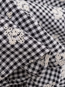 Détail du tissu à carreaux noir et blanc avec broderie florale blanche sur une chemise