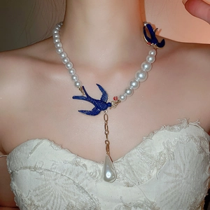 Macro detail of a pearl necklace set featuring blue swallow charms and a water drop pendant