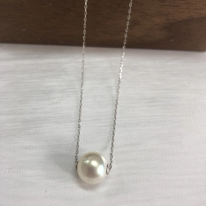 Close-up of a lustrous white pearl pendant on a fine silver chain over white fabric