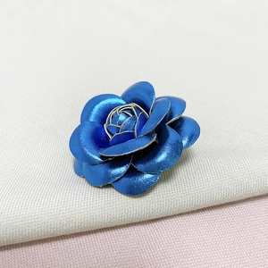 Close-up of blue metallic rose brooch on soft textured fabric background