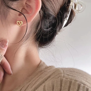 Close-up of heart-shaped hollow earrings in gold finish worn on a female ear