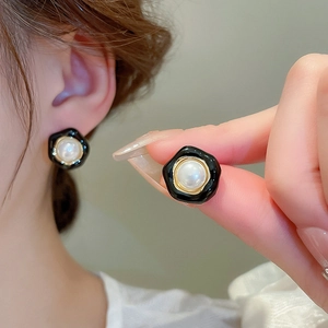 Macro detail of irregular black pleated earrings with pearl center and golden metal edges