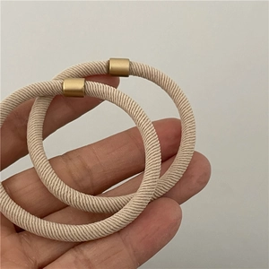 Close-up of cream elastic hair ties with matte gold metal buckles held in hand