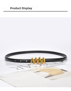 Detail of slim black leather belt with golden wavy buckle on magazine background