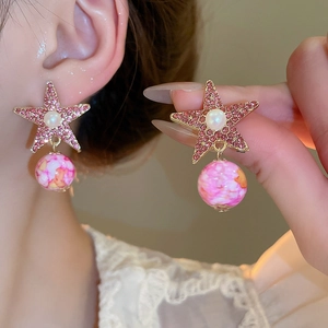 Close-up of star earrings with pink rhinestones, white pearls, and hanging spherical beads