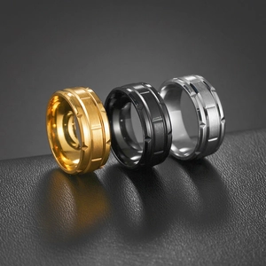 Three men's brushed titanium steel rings in gold, black, and silver with gear grooves