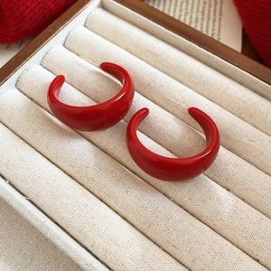 Close-up of glossy red C-shaped hoop earrings on beige velvet jewelry box background