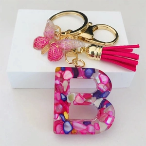 Close-up of resin letter B keychain with colorful stones, pink butterfly, and suede tassel