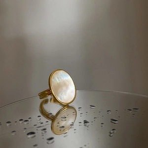 Detailed view of oval mother of pearl ring with gold band reflecting on wet mirror surface