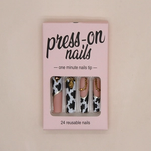Detail of cow print press-on nails with golden rhinestones and chain accents in packaging