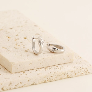 Detailed view of silver snake-head hoop earrings with crystals on beige stone blocks